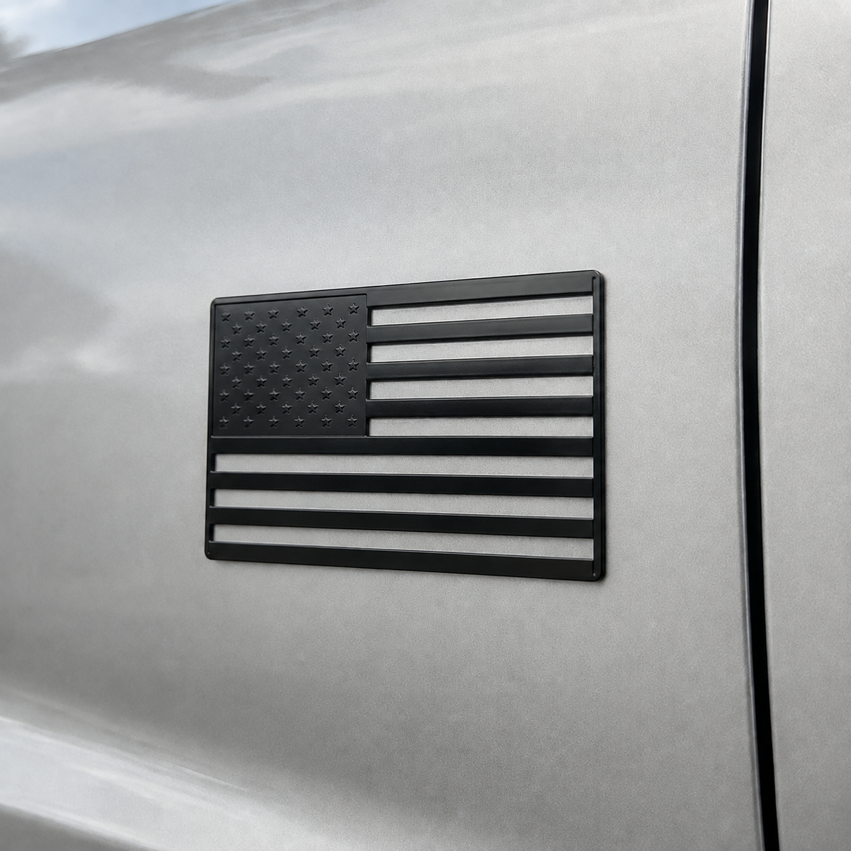 Black 3 by 5 inch US flag metal car emblem installed on a silver vehicle